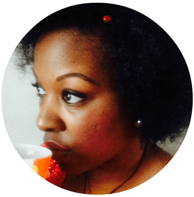 Photo of Tracey Rogers, astrologer and horoscope writer. She's wearing an afro, a red polka dot shirt, and is drinking from a mug of tea.