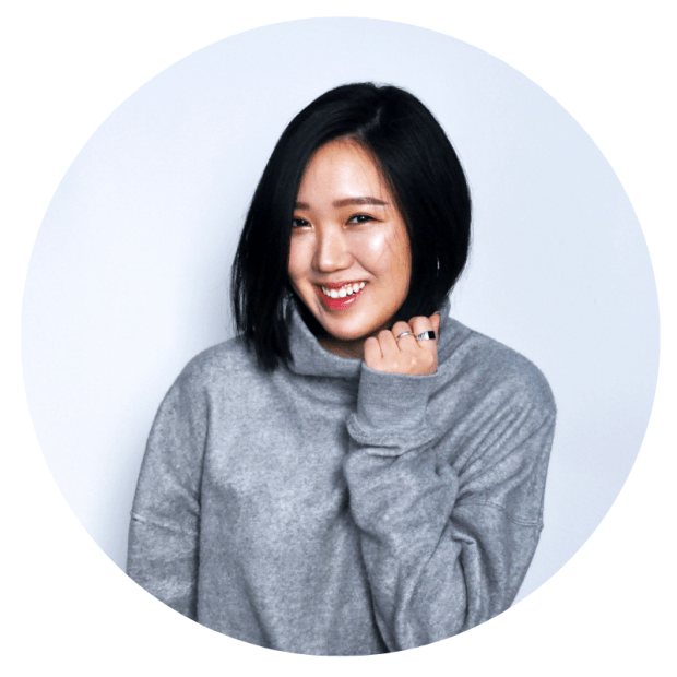 Team Sesi. Headshot of Jamie Yu, lead layout designer. She's an Asian woman, wearing a gray turtleneck. Her black hair is short, and she's smiling for the camera with one hand gently pulling on the neck of the sweater.