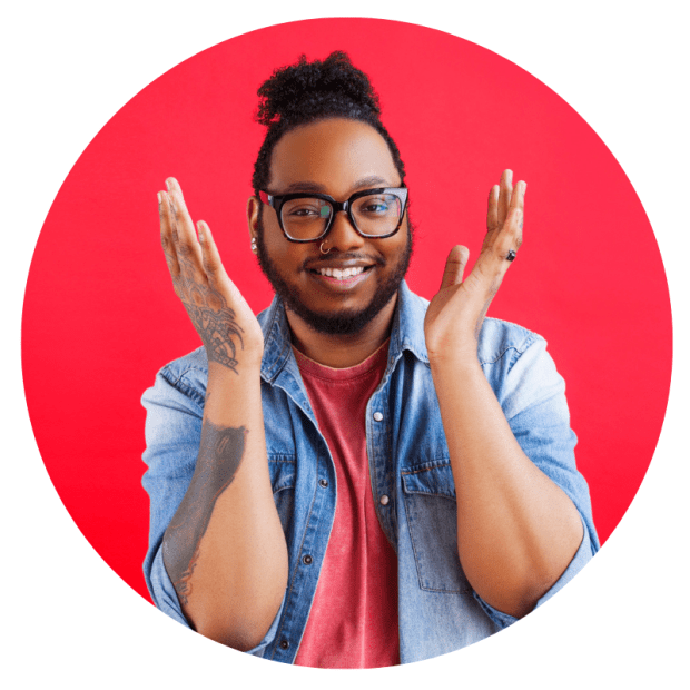 Headshot of Sire Leo Lamar-Becker, contributing writer and photographer. He's a Black man and is wearing is hair in a curly bun; he's also wearing black glasses, a nose ring, and a salmon-colored T-shirt with a light wash denim jacket over that. He's standing against a red background, holding his hands up by his face.