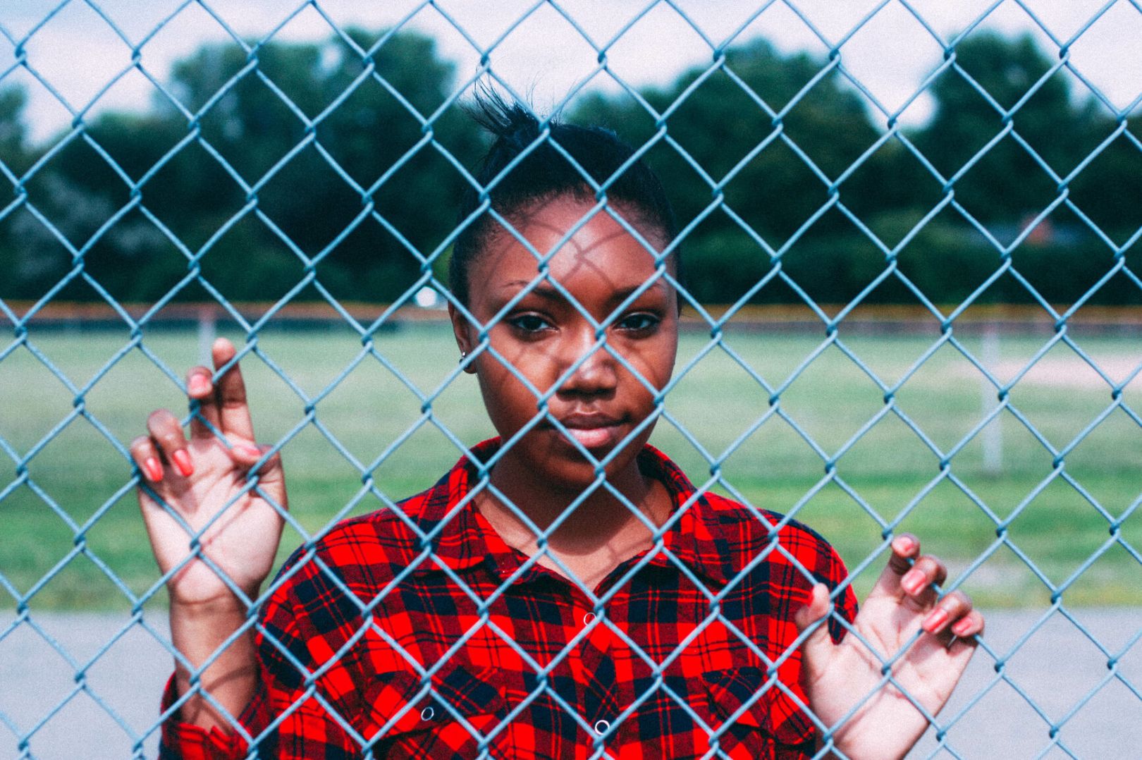 Black teen girl standing against fence, holding on to chain links