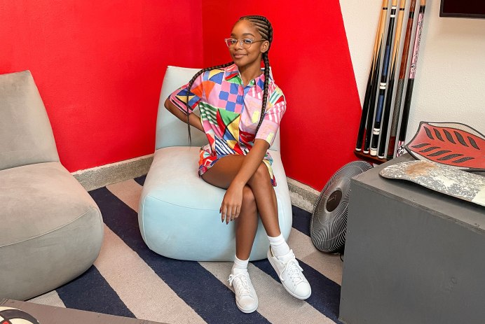 Marsai Martin sitting in blue chair of renovated garage on new show Remix My Space with Marsai Martin. She's wearing two braids and a colorful, geometric patterened T-shirt dress