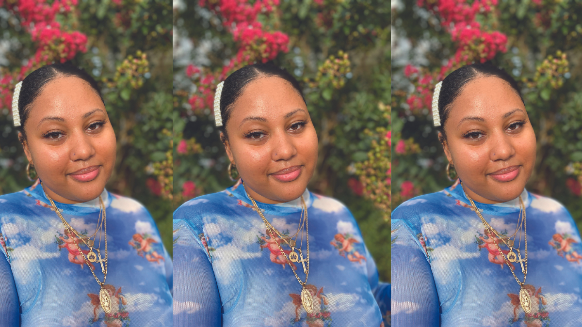 Elsa Mengistu standing outside looking at the camera, Her hair is pulled back with a pearl barrette on one side. She's wearing a blue patterned top.