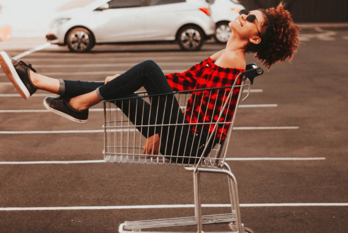 Black teen girl sitting in shopping cart laughing