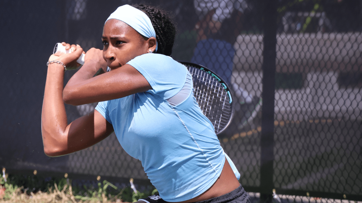 Coco Gauff wearing a blue top and white, sports headband as she gets ready to swing her tennis racket