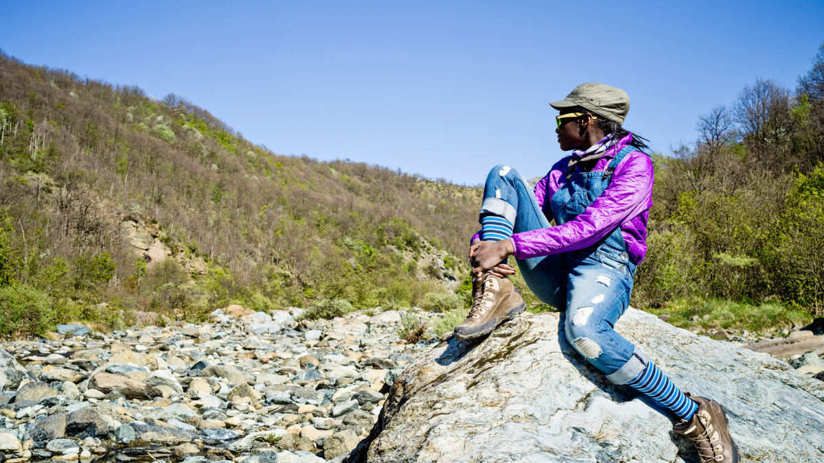 Black teen girl sitting on top of a rock out in nature