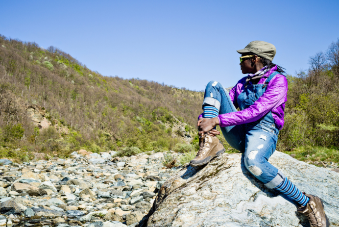Black teen girl sitting on top of a rock out in nature