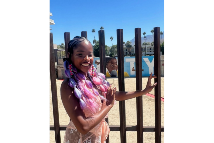 Amanda Gorman is wearing pink and purple braids and standing in front of a mural of herself commissioned in Palm Springs, California
