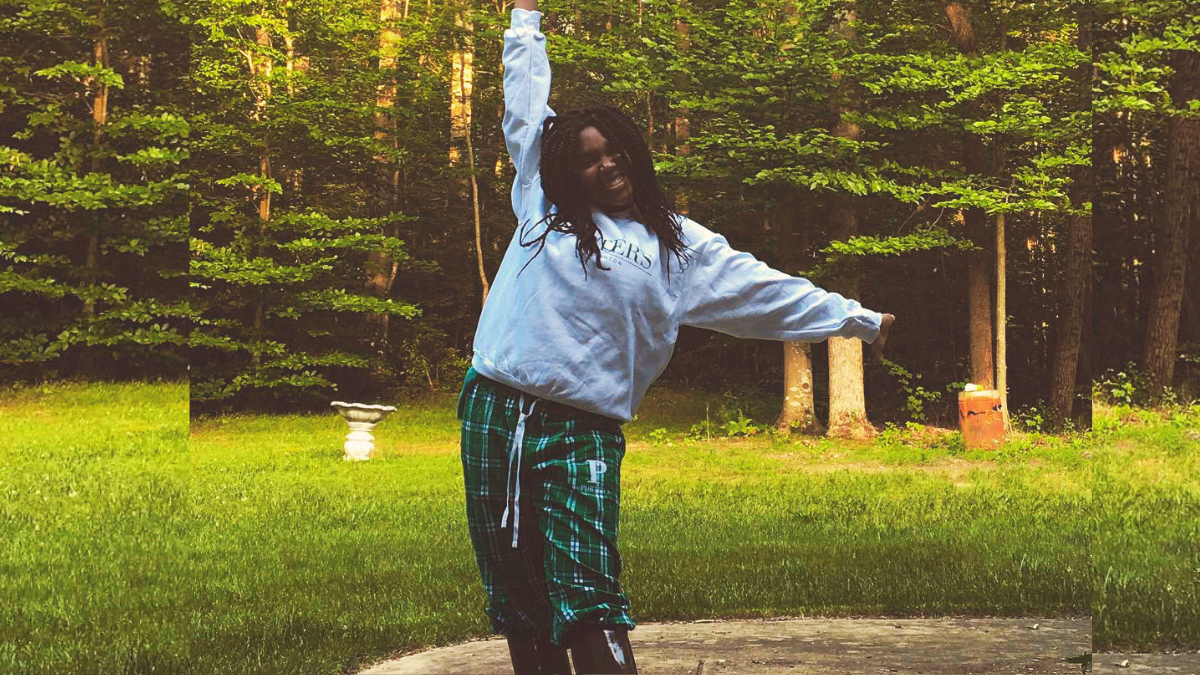 Black teen girl, Shani Vigilant, standing outside smiling and wearing her gray Miss Porter's sweatshirt with plaid Miss Porter's sweatpants and black rain boots. Her hair is in long twists