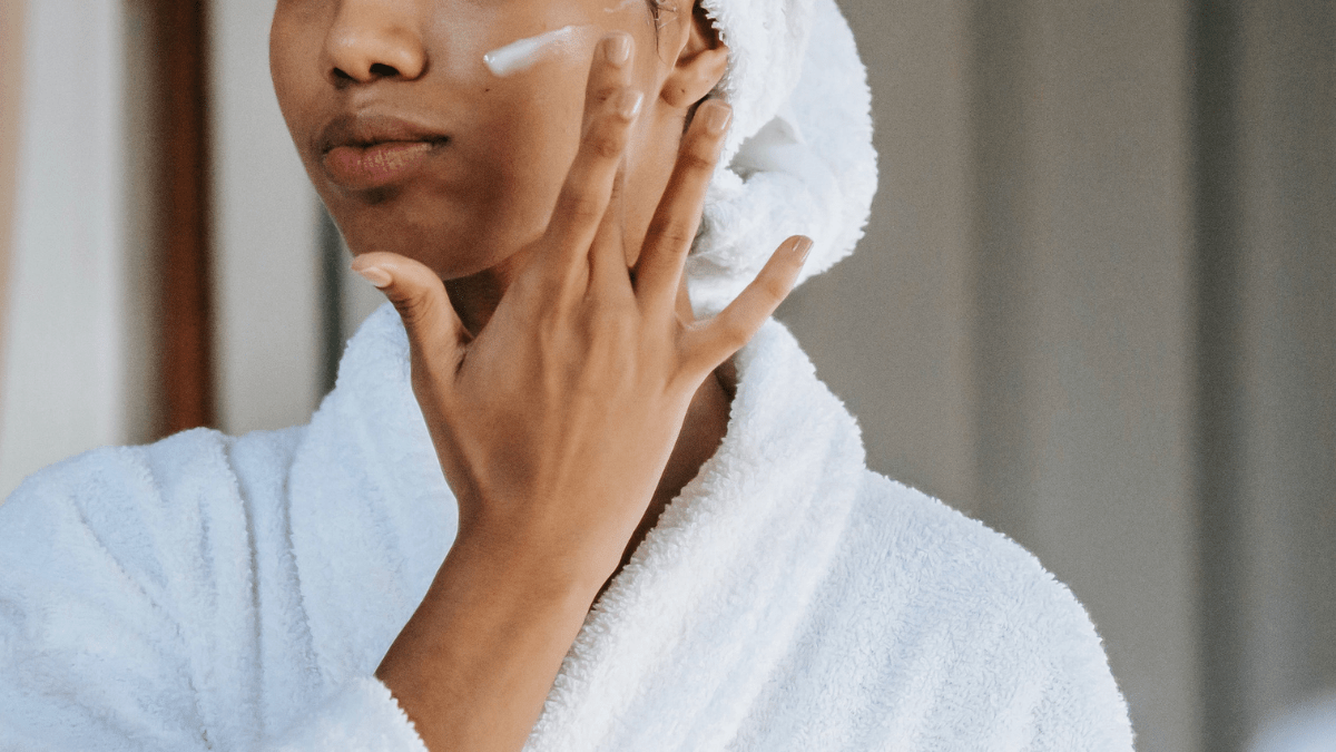 Black teen girl applying face cream while wearing white robe and white towel on head