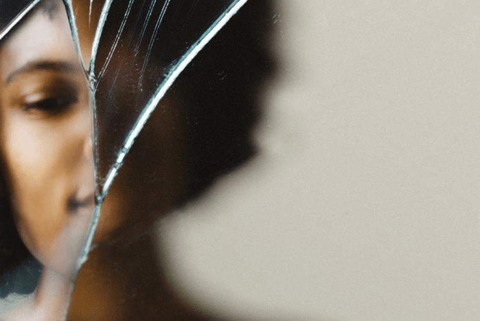 sad Black teen girl looking into cracked mirror