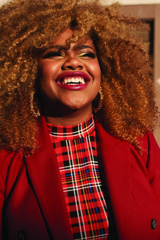 Dara Renee smiling with curly 'fro, wearing red plaid mock turtleneck and red coat