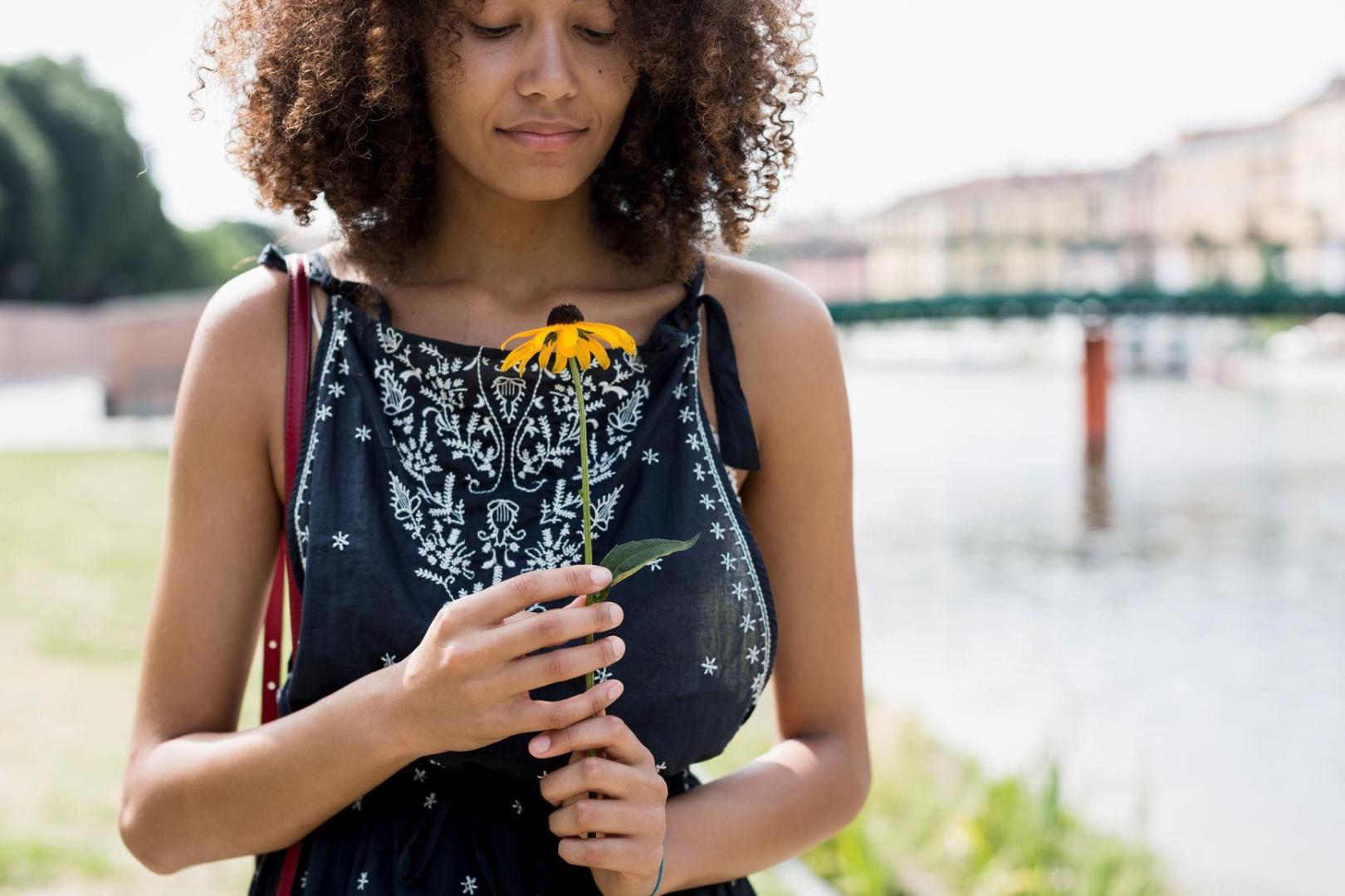 Black teenage girl with curly afro looking a little crestfallen holiding a drooping sunflower