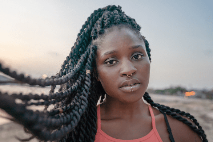 African-american teen girl with Senegalese twists and nose and lip piercings on her face on the beach at sunset