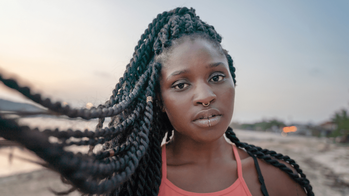 African-american teen girl with Senegalese twists and nose and lip piercings on her face on the beach at sunset